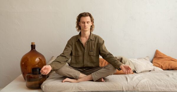 Person sitting on a mat in a relaxed seated pose in a bright, calm room
